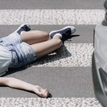 Image of a person laying in a crosswalk with a car in the shot.