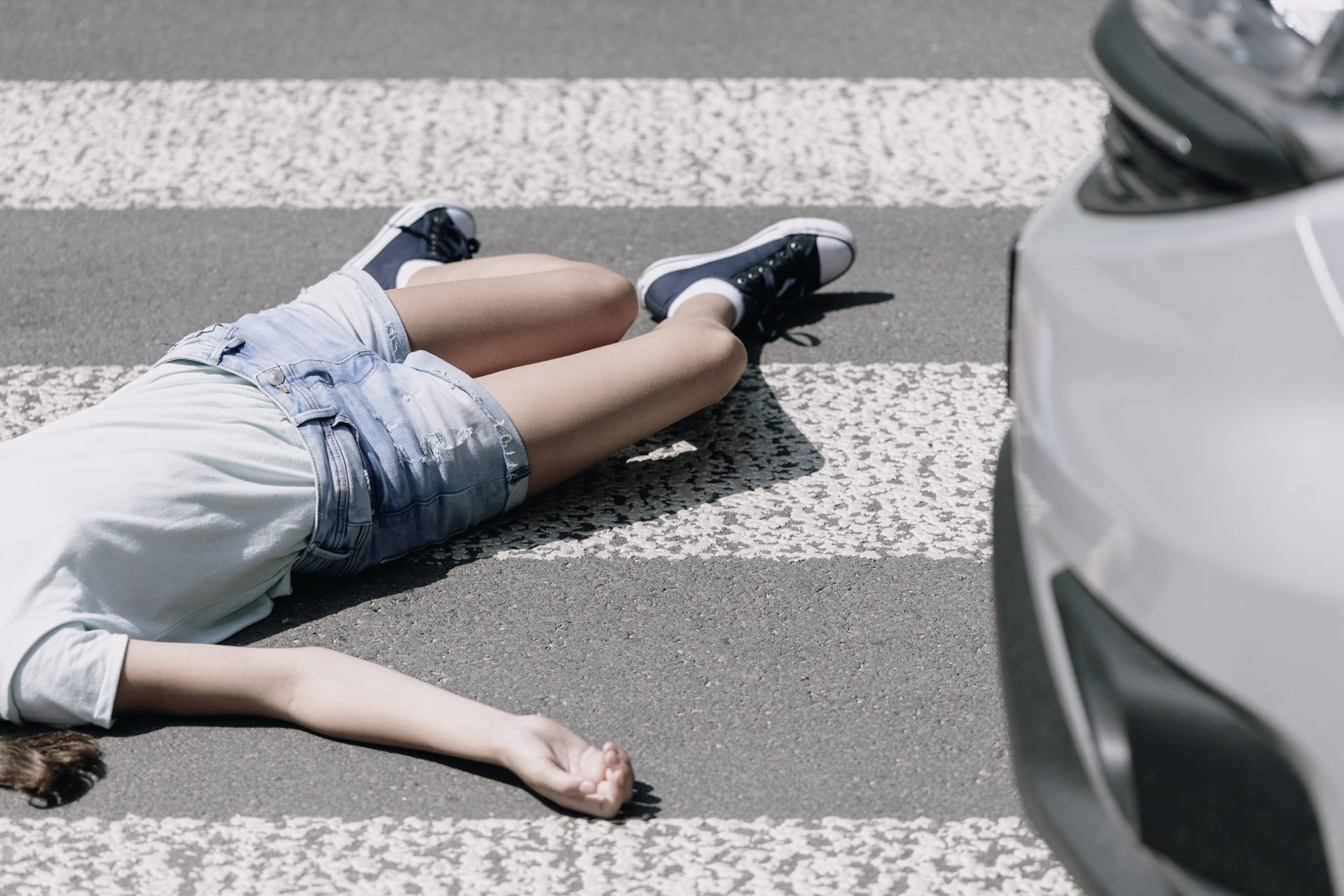 Image of a person laying in a crosswalk with a car in the shot.