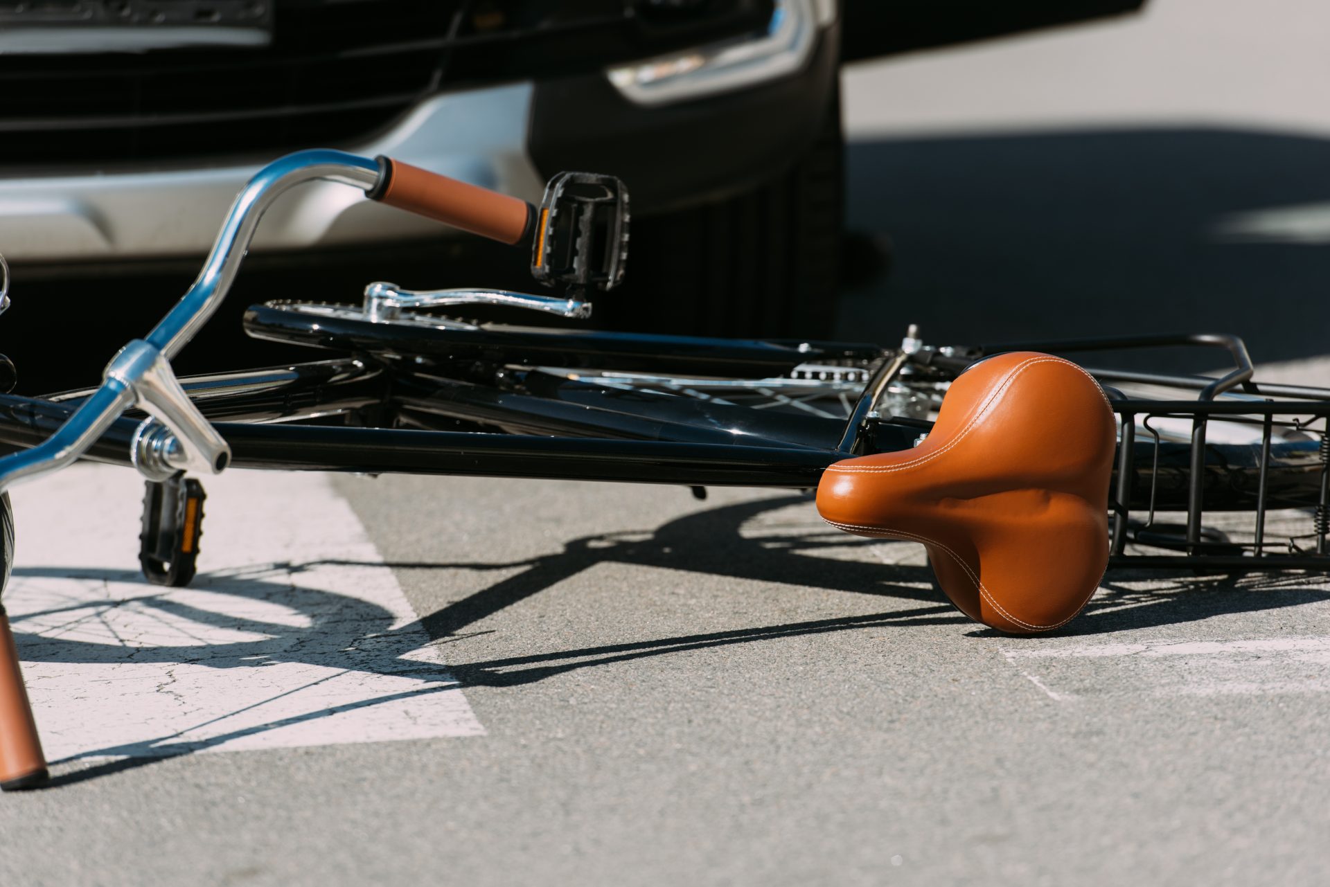 A bicycle lying on the ground under a car that hit it.